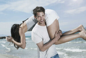 spain-majorca-young-man-carrying-woman-on-shoulders-at-beach-WESTF017131